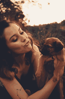 a woman with a constellation tattoo on her arm holds a brown puppy