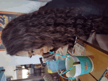 a woman sits at a table drinking a smoothie from a bucket with a straw