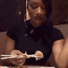 a woman is sitting at a table with chopsticks eating sushi .