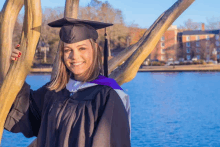 a woman in a graduation cap and gown is standing next to a tree