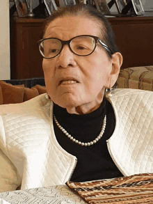 an older woman wearing glasses and a pearl necklace sits at a table