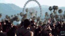 a blurry picture of a crowd of people at a music festival with a ferris wheel in the background .