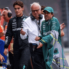 a man in a green petronas jacket talks to another man in a white shirt