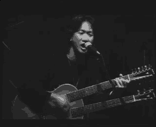 a man is singing into a microphone while holding a guitar in a black and white photo .