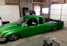 a green truck is parked in a garage with a man in the driver 's seat giving a thumbs up