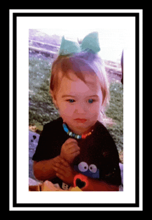 a little girl with a blue bow on her head is wearing a cookie monster shirt