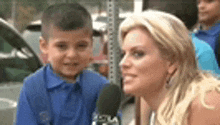 a woman is talking to a young boy in a blue shirt while holding a microphone .