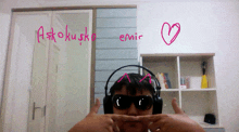 a person wearing headphones and sunglasses has a heart drawn on the wall above them that says " astokusk "