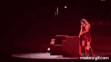 a woman is standing on a stage in a dark room holding a red object .