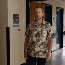 a man in a hawaiian shirt stands in a hallway with a poster on the wall that says ' a '