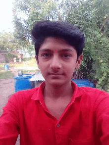 a young man in a red shirt takes a selfie in front of blue barrels