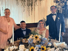 a bride and groom are sitting at a table with their parents at their wedding reception .