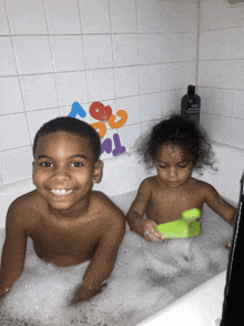 a boy and a girl are taking a bath in a bathtub with foam toys on the wall