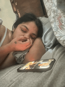 a woman laying on a bed looking at a cell phone with a picture of a person on it