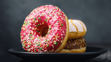 a donut with pink frosting and sprinkles sits on a plate