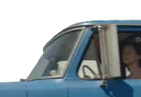 a woman sits in the driver 's seat of a blue truck with the door open