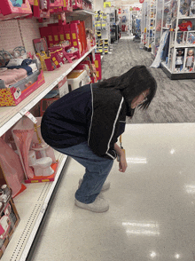 a woman is squatting down in a store looking at a toilet