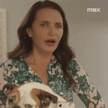 a woman in a floral shirt is holding a dog with a max logo in the corner
