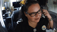 a woman wearing glasses and a pittsburgh steelers shirt talks on a phone