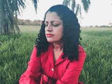 a woman in a red shirt sits in the grass