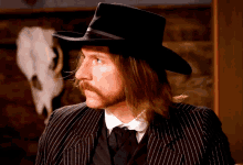 a man with long hair and a mustache is wearing a black hat