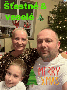 a man and woman are posing for a picture in front of a christmas tree with merry xmas written on it