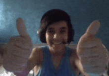 a young boy wearing headphones and a blue tank top is giving two thumbs up .