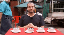 a man sits at a table with three bowls and saucers in front of a sign reading rai 2 hd