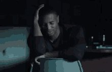 a man is sitting in a chair in a dark room with his head in his hands .