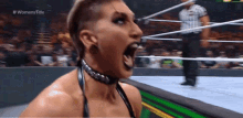 a woman is screaming in a wrestling ring while a referee stands in the background .