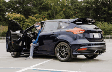 a man sits in the driver 's seat of a blue ford