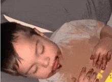 a little boy is sleeping on a bed with a piece of cake in his mouth .