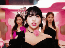 a group of girls are standing in a pink room . one of the girls is wearing a black dress and a pink flower .