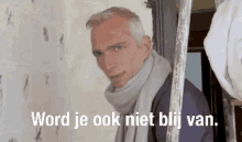 a man with a scarf around his neck is standing in front of a wall with the words word je ook niet bij van .