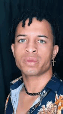 a young man wearing a necklace and earrings with a cross on his ear is looking at the camera .