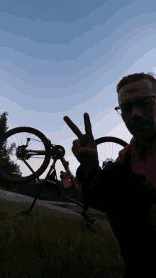 a man giving a peace sign with a bicycle in the background