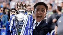 a man in a suit and tie is holding a soccer trophy .