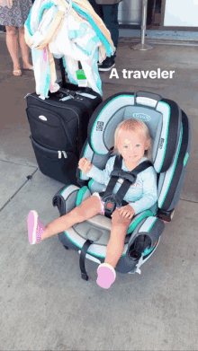 a little girl is sitting in a graco car seat next to a suitcase