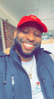 a man wearing a red hat and a white shirt with a rose on it smiles for the camera