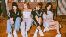 four girls are sitting on a wooden floor in front of a book shelf