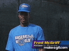 a man in a baseball cap is pointing at the camera while wearing a blue shirt that says baseball world .