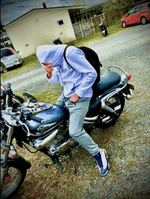 a man wearing a hoodie is standing next to a blue motorcycle