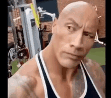 the rock is taking a selfie in a gym while wearing a tank top .