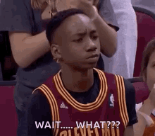 a young man in a cleveland cavaliers jersey is sitting in the stands with his hand on his head .