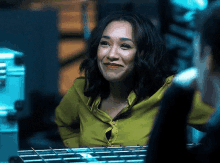 a woman in a yellow shirt is smiling and looking at the camera while sitting in a dark room .