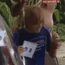 a young boy in a blue shirt is holding a piece of paper with a name tag on it .