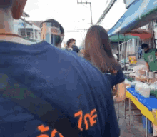 a man wearing a blue shirt with the number 7 on it is standing in front of a market .