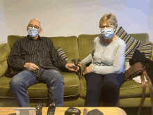 a man and a woman wearing masks sit on a green couch