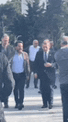 a group of men in suits are walking down a street .