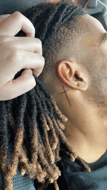 a man with dreadlocks has a tattoo of a cross behind his ear